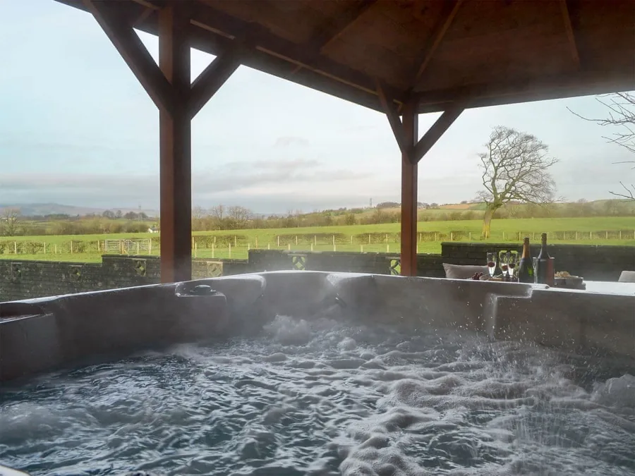Steaming hot tub beneath a timber shelter overlooking green countryside